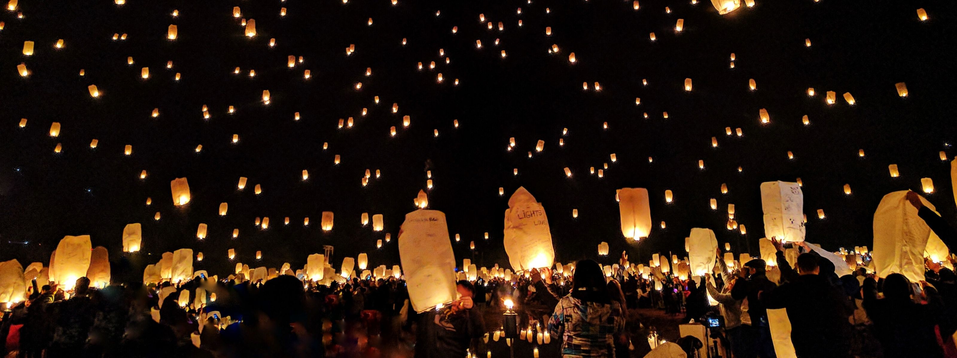 Setki lampionów świetlnych puszczane przez ludzi o zmroku.