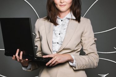 Elegancko ubrana rekurterka z laptopem w rękach na czarnym tle z białymi strzałkami.