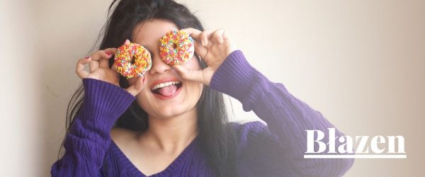 Archetyp Błazen: szeroko uśmiechnięta dziewczyna, żartobliwie przykłada donuty do oczu.