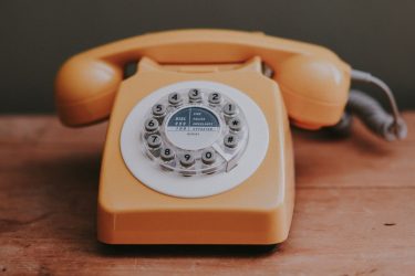 Pomarańczowy, stary, nakręcany telefon umieszczony na drewnianym blacie