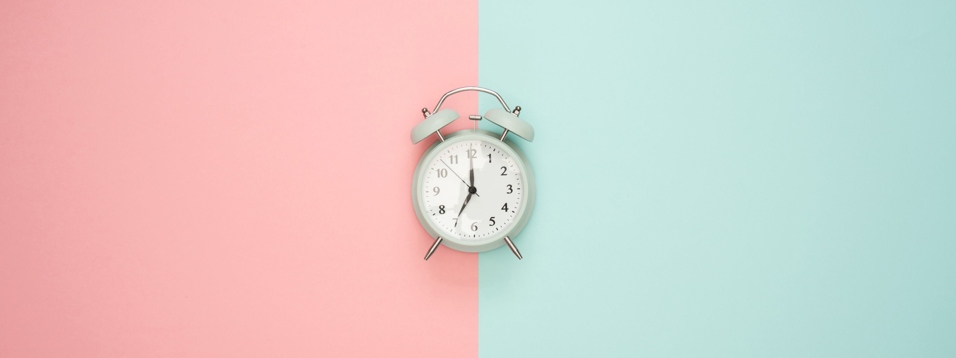 Szary, klasyczny zegar - budzik na tle w dwóch kolorach - różowym i niebieskim