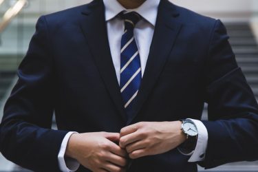 Elegancko ubrany mężczyzna, biznesmen - granatowy garnitur, krawat w paski, markowy zegarek.