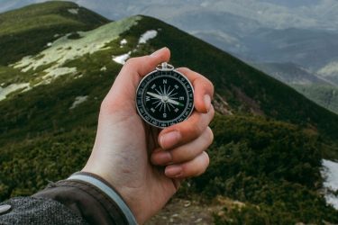 Kompas trzymany w dłoni wędrowcy na tle trawiastych, górskich szczytów