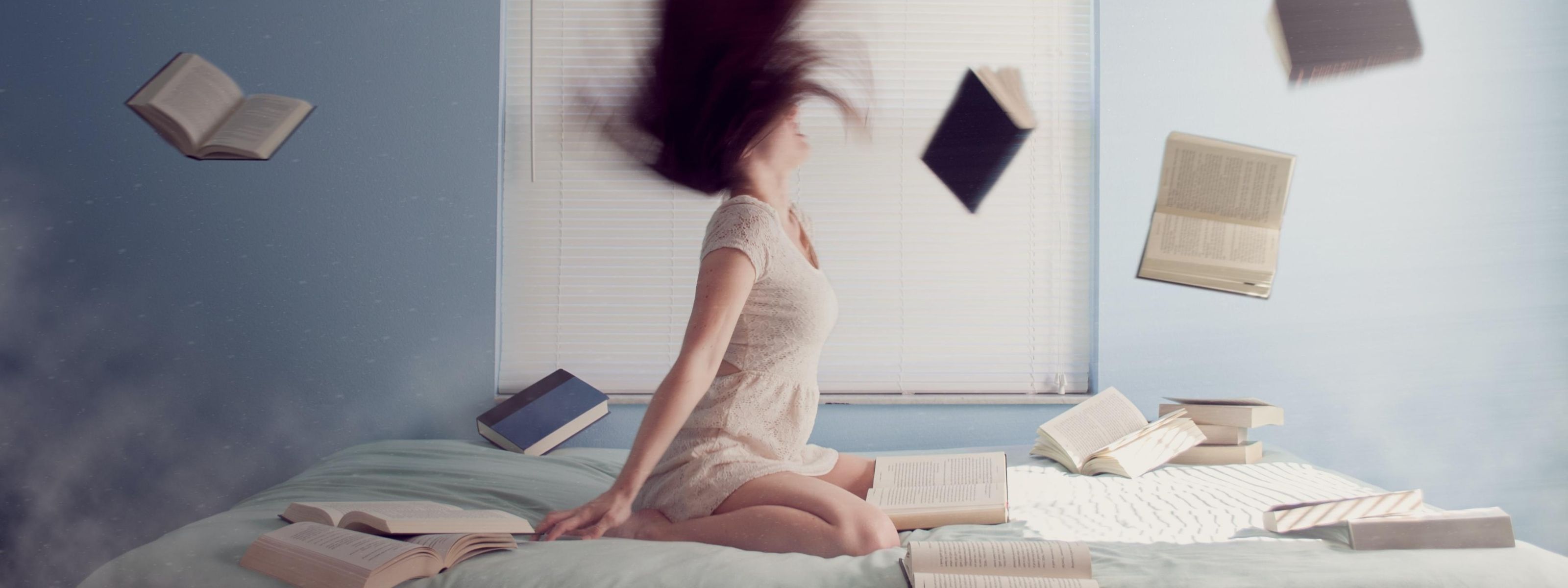 Dziewczyna siedzi na łóżku, a wokół niej unoszą się książki.