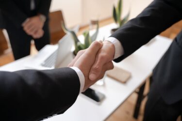Dwaj mężczyźni w garniturach ściskają sobie dłonie, przypieczętowując barter