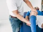 Fizjoterapeuta masuje nogę piłkarza na stole do masażu w szpitalu