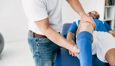 Fizjoterapeuta masuje nogę piłkarza na stole do masażu w szpitalu