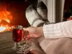 Kobieta leżąca przy kominku z herbata w dłoni - hygge