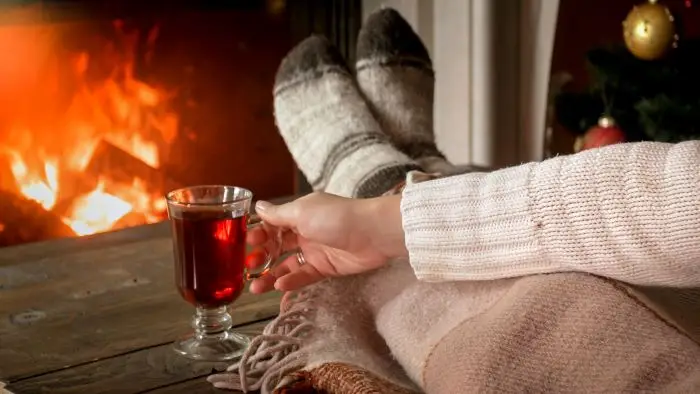 Kobieta leżąca przy kominku z herbata w dłoni - hygge