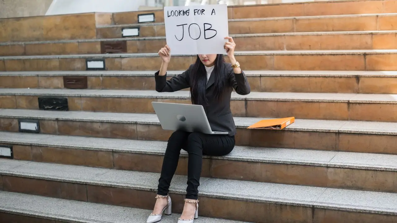 Jak szukać pracy - kobieta siedząca na schodach i trzymająca w dłoniach napis "looking for a job"