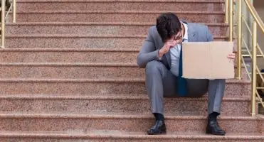 Smutny, elegancko ubrany mężczyzna siedzący na schodach z kartonem
