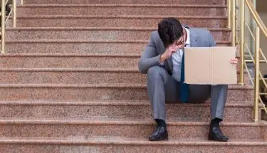 Smutny, elegancko ubrany mężczyzna siedzący na schodach z kartonem