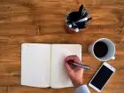 Podanie o pracę - mężczyzna piszący w notesie, na biurku kawa i telefon