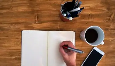 Podanie o pracę - mężczyzna piszący w notesie, na biurku kawa i telefon