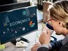 Biegły rewident - mężczyzna pijący kawę przed komputerem, na ekranie napis "economics"
