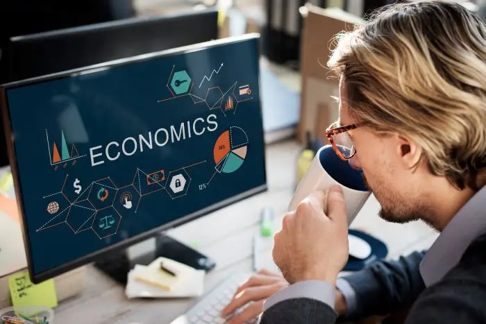 Biegły rewident - mężczyzna pijący kawę przed komputerem, na ekranie napis "economics"