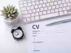 Dokuemnt CV na blacie, obok zegar i klawiatura komputera