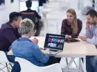 Microsoft teams - ludzie siedzący przy biurku w pracy, kobieta trzyma laptopa