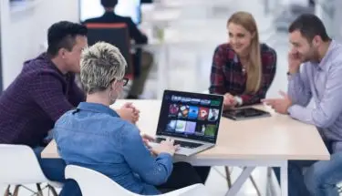 Microsoft teams - ludzie siedzący przy biurku w pracy, kobieta trzyma laptopa