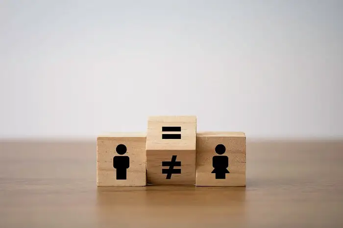 Seksizm w miejscu pracy - drewniane klocki ukazujące ikonki mężczyzny i kobiety i zmieniający się między nimi znak równości