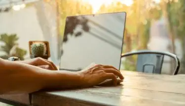 Człowiek używający myszy komputerowej pracujący z laptopem na stole