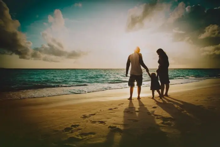 Szczęśliwa rodzina z dzieckiem bawiącym się na plaży o zachodzie słońca