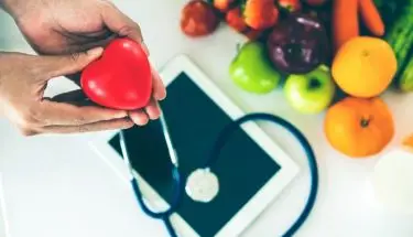 Jak sprawdzić czy jest się ubezpieczonym - figurka serca trzymana w dłoni, nad sprzętem medycznym, tabletem i owocami