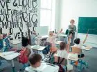 Dzieci siedzące w klasie podnoszą ręce, aby podejść do tablicy