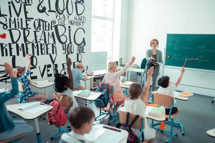 Dzieci siedzące w klasie podnoszą ręce, aby podejść do tablicy