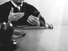 Prokurator - elegancko ubrany mężczyzna siedzący przy biurku, trzymający w dłoni telefon