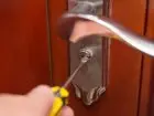 Ślusarz - zdjęcia zamka w drzwiach, który ktoś próbuje naprawić śrubokrętem