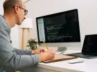 Programista siedzący przed ekranem komputera, na którym widać kod