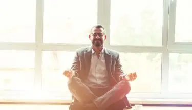 Jak się uspokoić w pracy - mężczyzna w garniturze, siedzący w pozycji lotosu