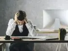 Pracoholizm - mężczyzna przy biurku, trzymający się za głowę