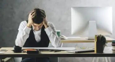 Pracoholizm - mężczyzna przy biurku, trzymający się za głowę