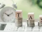 Skala podatkowa 2024 - napis tax na stosach monet, w tle zegar