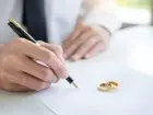 Mężczyzna podpisujący dokument, na nim położone obrączki