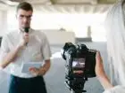 Mężczyzna stojący przed kamerą z notatkami i mikrofonem