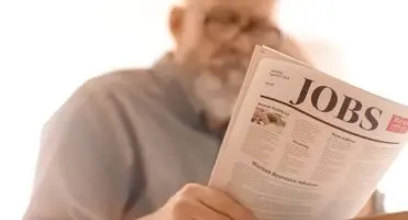 Mężczyzna czytajacy gazetę z napisem "jobs"