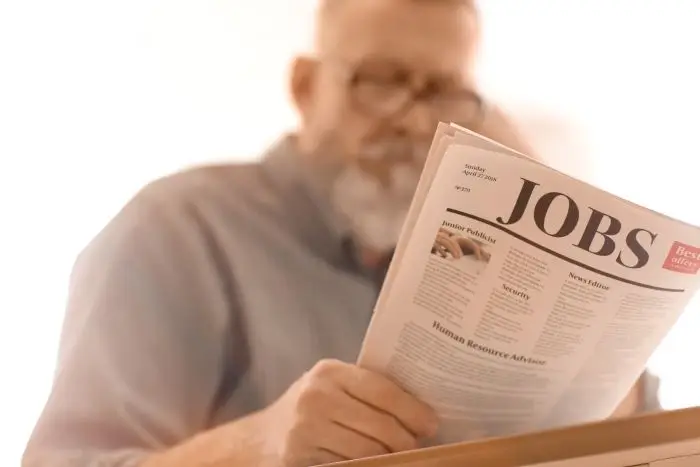 Mężczyzna czytajacy gazetę z napisem "jobs"