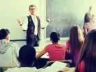Nauczyciel stojący przy tablicy w sali lekcyjnej, patrzą na niego dzieci w ławkach