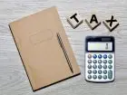 Notatni, długopis, kalkulator i klocki układające napis "tax" na blacie