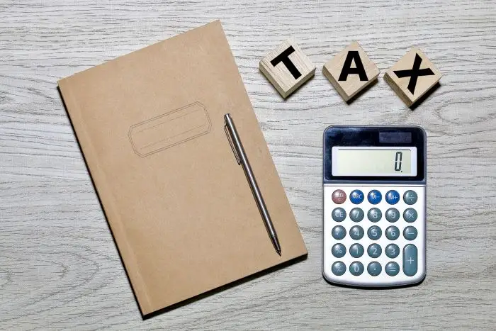 Notatni, długopis, kalkulator i klocki układające napis "tax" na blacie