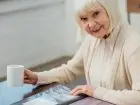 Kobieta, seniorka siedząca przy stole z kubkiem, usmiechnięta