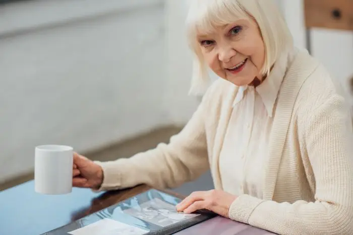 Kobieta, seniorka siedząca przy stole z kubkiem, usmiechnięta