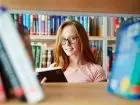 Studentka w bibliotece, w okularach, trzyma książki