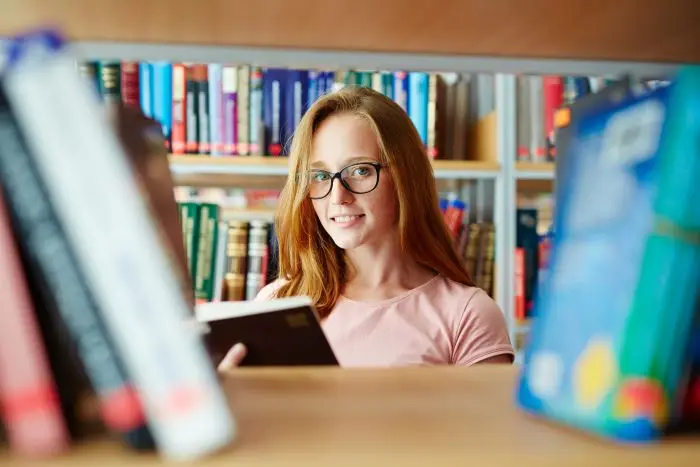 Studentka w bibliotece, w okularach, trzyma książki