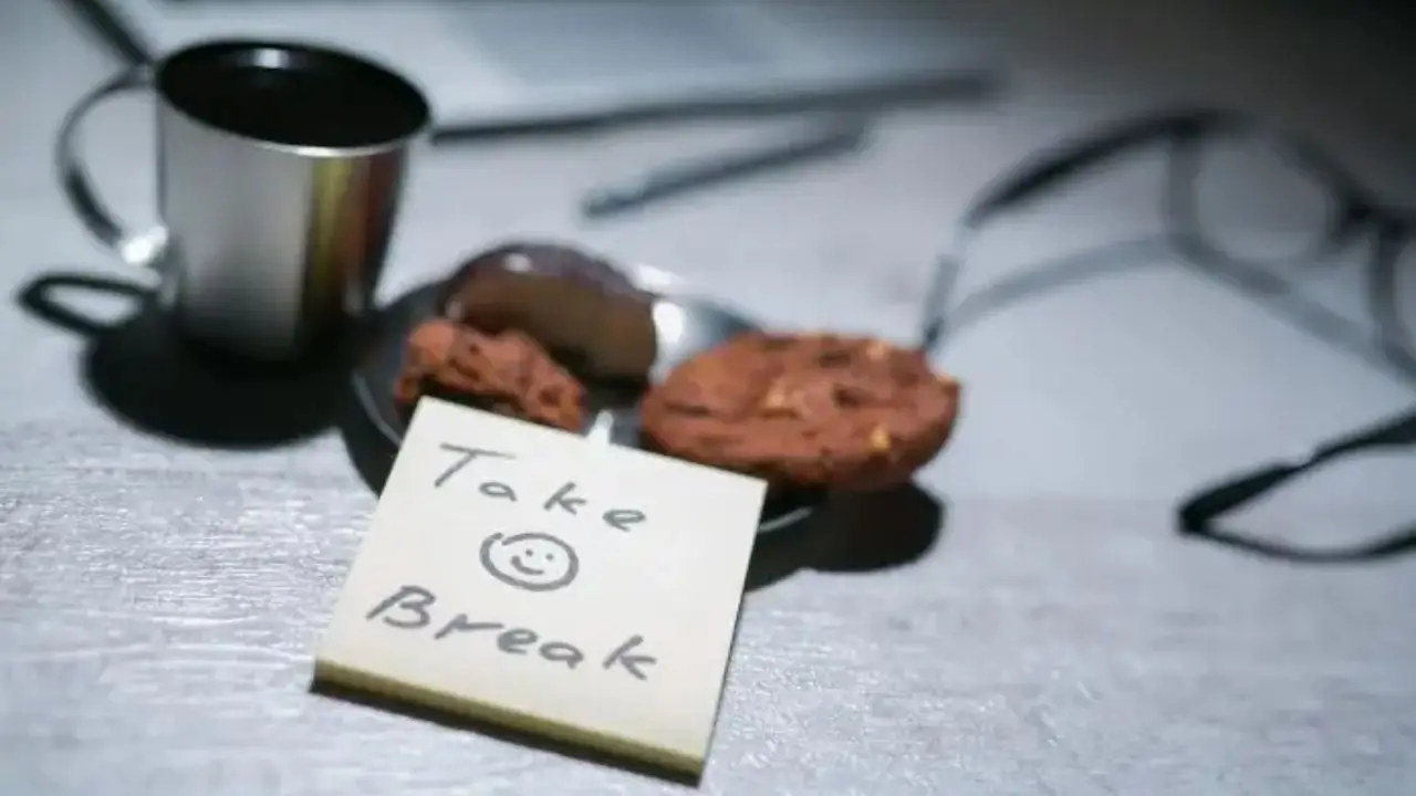 Biurko, a na nim kubek z kawą, talerz z ciastkami i kartka z napisem "take break"