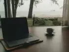 Laptop i kawa na biurku, w tle okno, a za nim morze