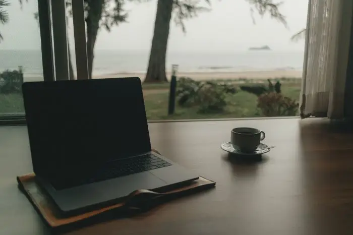 Laptop i kawa na biurku, w tle okno, a za nim morze